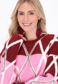 Virkat tröja med ett geometriskt mönster i röd, rosa och vit, med silverdetaljer. Naturliga fibrer skapar en mjuk textur.