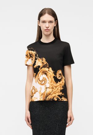 Femeie purtând un tricou cu mâneci scurte alb-negru cu modele ornamentale aurii în formă de spirale și o fustă texturată întunecată, pe un fundal simplu.