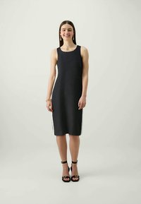 Melnas adītas bezpiedurkņu kleitas taisna silueta, ar sānu tekstūrām un bezšuvju dizainu. Modelis valkā melnas kurpes ar augstiem papēžiem.