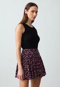 Schwarzes, geripptes Tanktop kombiniert mit einem ausgestellt Minirock, der einen schwarzen Hintergrund und ein lebhaftes Blumenmuster in Pink und Weiß hat.