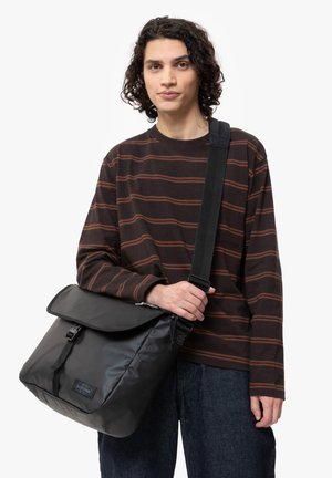 Zwarte messenger bag met een klep sluiting en een verstelbare schouderband. Heeft een gestructureerd oppervlak en een logo op de voorkant.