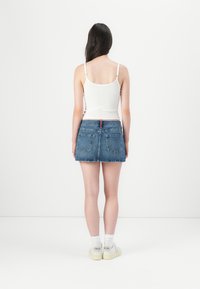 Balta tank top, mėlyna džinsinė mini sijonas su užpakalinėmis kišenėmis, tiesus apatinis kraštas, dėvima su baltomis kojinėmis ir šviesiais sportbačiais, matoma iš nugaros.