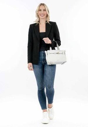 White handbag with structured shape, silver hardware, and top handles. Model wears a black blazer, fitted top, and blue jeans with sneakers.