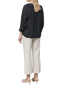 Zwarte blouse met kraag en driekwart mouwen, met een gedrapeerde achterkant, gecombineerd met crèmekleurige wijde broek en witte hakken.