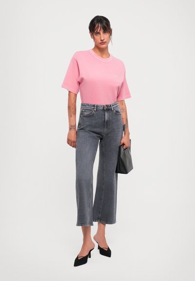 Light pink short-sleeve t-shirt, gray wide-leg jeans, black pointed heels, and a black clutch. Simple design with a relaxed fit and subtle stitching.