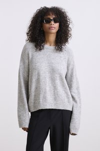 Grijze gebreide trui met een losse pasvorm, ronde halslijn en lange mouwen, gecombineerd met zwarte pantalons. Zachte textuur met een licht fuzzy afwerking.
