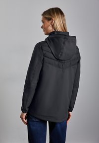 Svart huva jacka med vadderad övre del, som har en slät yta och en något avslappnad passform. Matcher med jeans i denim.