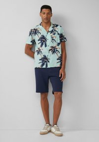 Een lichtblauw shirt met korte mouwen en donkere palmbomenpatronen, gecombineerd met marineblauwe shorts en witte sneakers met beige accenten.