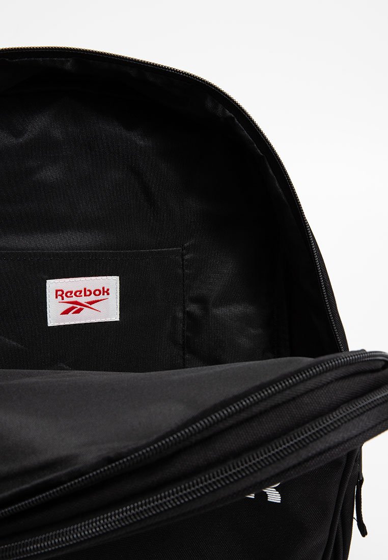 Mochila negra abierta para mostrar el bolsillo interior con una etiqueta de logo de Reebok en blanco y rojo cosida dentro.