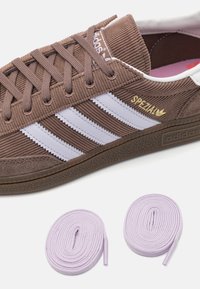 Bruna kordsvarta sneakers med vita ränder och guld "Spezial"-text. Inkluderar två lavendelfärgade skosnören, texturerad sula och stoppad tunga.