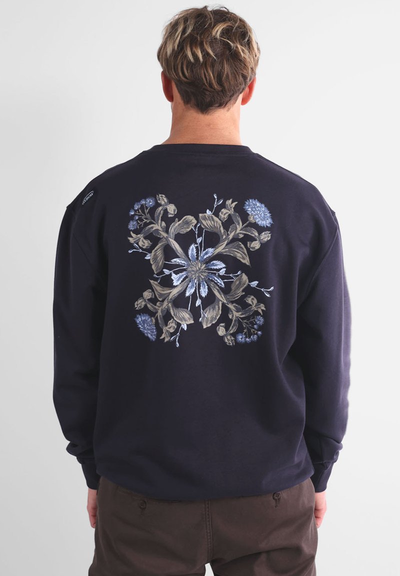 Sweatshirt marine avec motif floral brodé en bleu clair et beige, centré au dos. Manches longues, col rond, coupe standard.