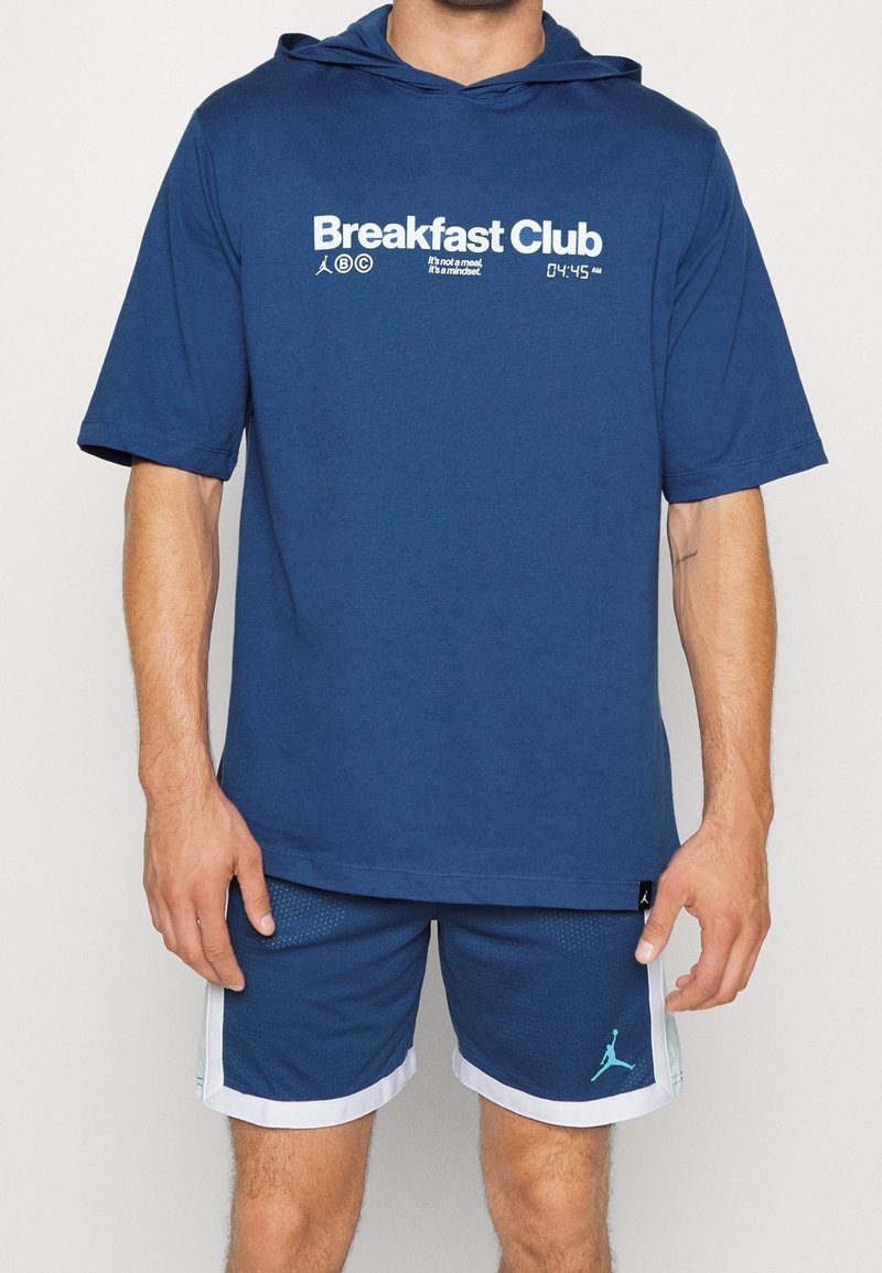 Dunkelblaues kurzärmliges Hoodie mit weißem "Breakfast Club"-Text. Kombiniert mit dunkelblauen Shorts mit weißen Akzenten und dem Jordan-Logo.
