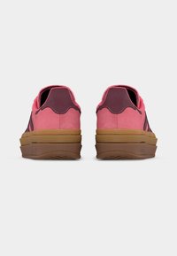 Ζευγάρι ροζ σουέντ sneakers χαμηλού ύψους με μαρουν αποχρώσεις και παχιά στρωματοποιημένη καφέ ελαστική σόλα, εμφανιζόμενα από πίσω σε λευκό φόντο.