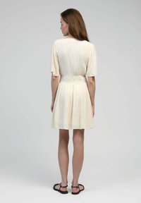 Robe courte crème avec une taille cintrée, des manches courtes et volantées, et une jupe évasée. Texture lisse avec de légères lignes verticales.