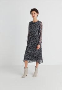 Μάξι φόρεμα με μακριά μανίκια σε διάφανο μαύρο ύφασμα με floral μοτίβα, ελαστική μέση και πτυχώσεις στη φούστα, συνδυασμένο με ανοιχτό γκρι μποτάκια μέχρι τον αστράγαλο.