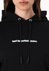 Felpa nera con cappuccio caratterizzata da logo ricamato bianco "karl lagerfeld jeans" sul petto, occhielli metallici e coulisse regolabile.