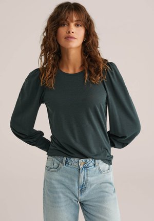 Donkergroene lange mouwen shirt met pofmouwen, ronde halslijn en zachte stof, gecombineerd met lichtblauwe high-waisted jeans.