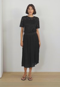 Černý krajkový top s krátkým rukávem, v kombinaci se skladanou černou midi sukni. Oblečení doplňují černé žabky. Jednoduchý a elegantní design.