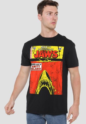 Black cotton t-shirt featuring a bold graphic print with “Jaws” in red and yellow, depicting a shark's open mouth against an orange background.