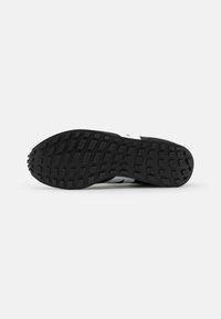 Black footwear sole featuring a textured rubber surface with a herringbone pattern and slight cushioning elements for traction.