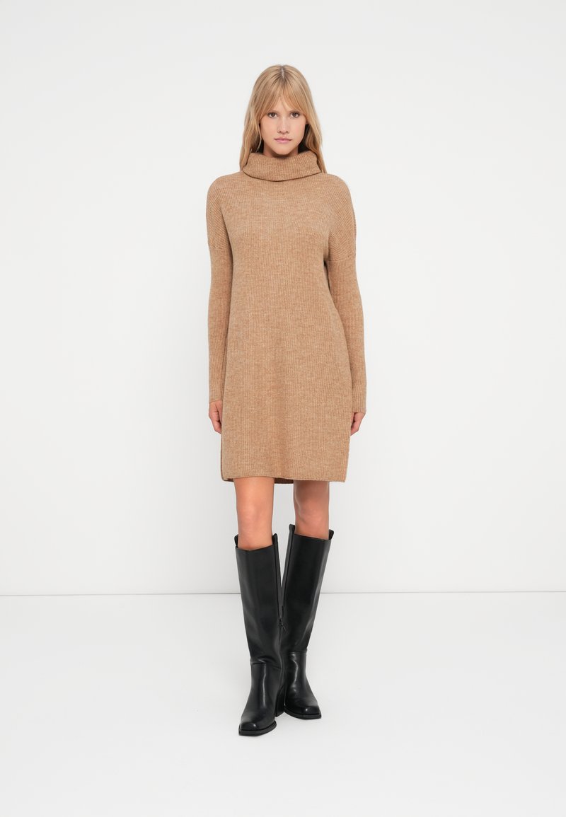 Abito maglione di colore cammello con collo a cowl alto e maniche lunghe, caratterizzato da una vestibilità comoda che arriva sopra il ginocchio.