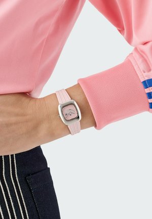 Kvadratna ura s srebrnim ohišjem in rožnato številčnico, z rožnatim gumenim pasom z rebrasto teksturo. Nosi se na zapestju.