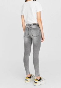 Jeans ajustados grises con efecto desgastado, diseño de cinco bolsillos y una cintura alta, combinados con una camiseta blanca y zapatillas de plataforma.