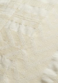 Beige strukturierter Stoff mit einem geometrischen Muster aus erhöhten Zickzack- und dreieckigen Designs. Weiche, gewebte Oberfläche mit subtiler Eleganz.