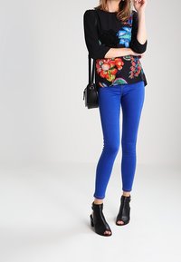 Svart topp med färgglada blommönster, trekvartsärmar, matchad med blå skinny jeans och svarta öppna ankelskor.