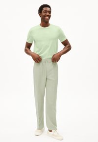 Lichtgroen t-shirt met korte mouwen, gecombineerd met lichtgroene, elastische broek. Gekocht met witte sneakers tegen een neutrale achtergrond.