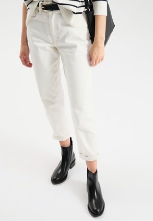 Białe jeansy w fasonie cropped z podwiniętymi nogawkami, w połączeniu z czarnymi botkami za kostkę. Materiał to dżins; strój ma swobodny, dopasowany wygląd.