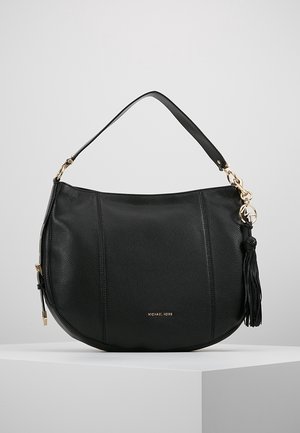 Sac à main en cuir noir en forme de demi-lune avec une bandoulière, des ferrures dorées, un détail pompon et un petit logo de la marque à l'avant.