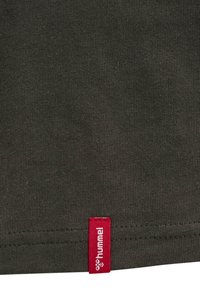 Tissu gris foncé avec une petite étiquette tissée rouge en bas de l’ourlet affichant un texte blanc et un logo d’abeille.