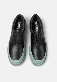 Scarpe in pelle nera con punta tondeggiante, dotate di suola in gomma verde menta e lacci. La soletta ha la scritta "CAMPER" stampata in bianco.