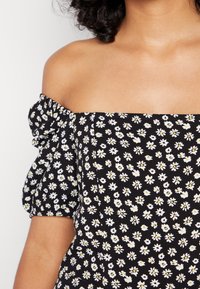 Top floral preto com ombros à mostra e mangas curtas bufantes, apresentando um padrão de margaridas brancas e amarelas. Tecido suave com uma silhueta ajustada.