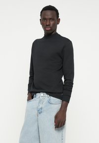 Felpa nera a maniche lunghe con scollatura rotonda e polsini a costine, abbinata a jeans di denim azzurro chiaro con vestibilità rilassata e chiusura a bottoni.