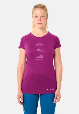 Jeune femme aux cheveux bouclés portant un T-shirt violet avec un motif de lignes de montagnes et le texte « Histoires des montagnes », associé à un pantalon bleu.