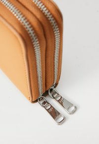 Hnědá kožená peněženka na zip se dvěma stříbrnými zipy a texturovaným povrchem. Obsahuje dvě přihrádky a zaoblené rohy.