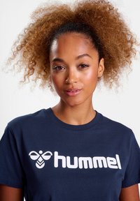 Marinblå t-shirt i bomull, med en stor vit "hummel" logotyp och abstrakt bi-design på framsidan, rund halsringning, kort ärm.
