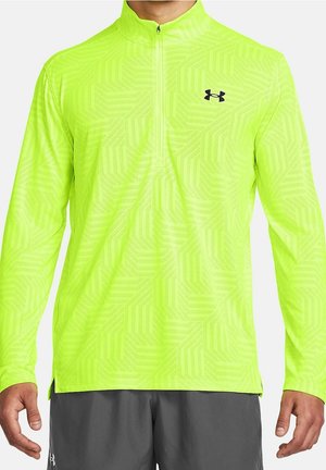 Man draagt een fel neongele lange mouw sportieve zip-up top met een subtiel geometrisch patroon en een zwart Under Armour-logo op de borst.