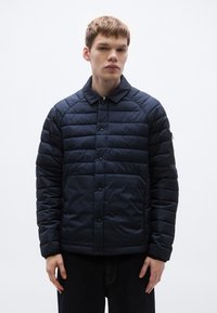 Granatowa ocieplana kurtka z kołnierzem, zapięciem na guziki i bocznymi kieszeniami; wyróżnia się teksturowaną tkaniną oraz kieszenią na rękawie na zamek.