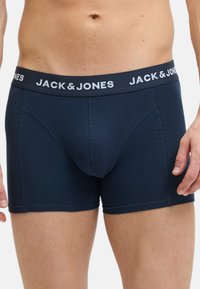 Boxer-briefs bleu marine avec une ceinture élastique blanche affichant le texte "JACK & JONES". Fabriqués en tissu lisse avec des coutures surpiquées.