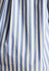 Blue and white striped fabric, featuring alternating vertical stripes in varying shades, with a smooth, slightly wrinkled texture.
