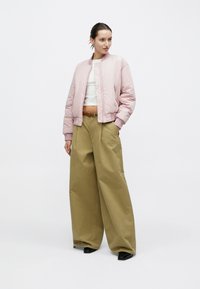 Giacca bomber rosa con polsini a costine, abbinata a pantaloni larghi color kaki. Top bianco corto visibile sotto, indossate scarpe nere con punta.