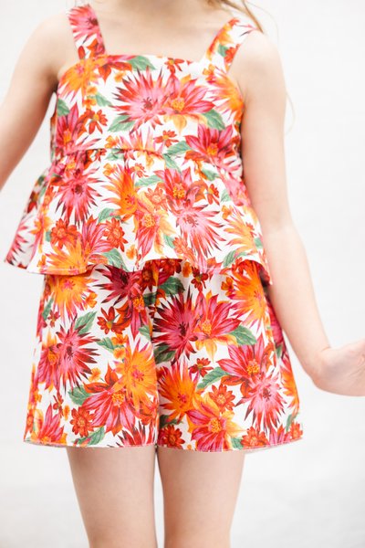 Σετ με δύο κομμάτια με λουλουδένιο μοτίβο, που περιλαμβάνει τοπ με πεπλούμ και σορτς. Κατασκευασμένο από ελαφρύ ύφασμα με έντονα κόκκινα, πορτοκαλί και πράσινα λουλούδια.