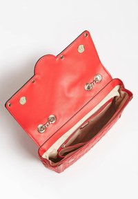 Punainen nahkainen käsilaukku, jossa on teksturoitu pinta, kullanväriset metalliosat ja aaltoileva läppä. Sisäpuolella on kerma-valkoinen vuori ja vetoketjutasku.
