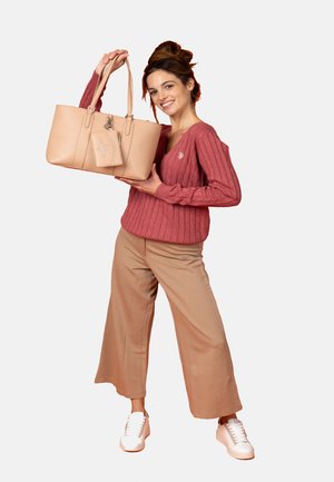 Beige tote bag med struktureret design og tekstureret overflade, udstyret med dobbelte håndtag og en aftagelig charm, parret med en lyserød ribbet sweater.