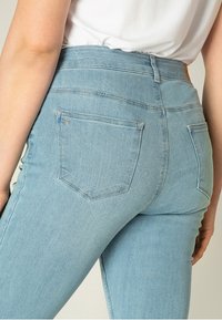 Lichtblauwe denim jeans met een hoge taille, voorzien van twee achterzakken en subtiele stikdetails. Glad oppervlak met een aansluitende pasvorm.