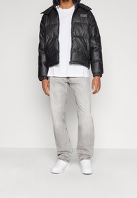 Czarna pikowana kurtka z zamkiem z przodu i elastycznymi mankietami, noszona na białej koszulce, zestawiona z jasnoszarymi dżinsami i białymi trampkami.