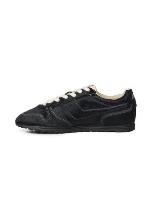 Zapatilla deportiva negra de corte bajo con cordones blancos, textura similar a piel, costuras blancas visibles y suela plana de goma sobre fondo blanco.
